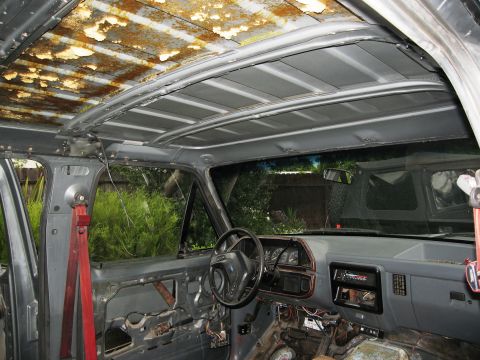 1986 Ford Bronco - The interior of a vehicle shows significant rust on the roof lining and disassembled door panels, indicating a state of disrepair.