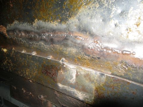 1986 Ford Bronco - This image shows a section of heavily rusted metal with prominent weld lines and some bubbling, indicating significant wear and tear.