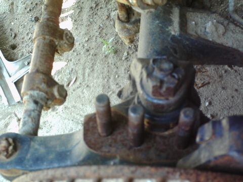 1990 Ford Bronco - Close-up view of heavily rusted vehicle suspension components, showing bolts and metal linkages.