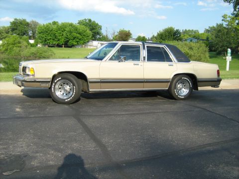 1988 Mercury Grand Marquis - A 1988 Mercury Grand Marquis sedan is parked on asphalt with a grassy area and trees in the background.