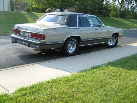 1988 Mercury Grand Marquis - A 1988 Mercury Grand Marquis is seen from a three-quarter front angle, parked on a sidewalk with a black vinyl roof.