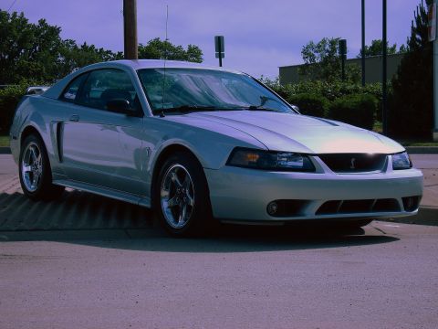 1998 Ford Taurus - A silver Ford Mustang Cobra is parked on a paved surface with trees and buildings in the background.