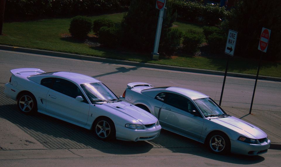 Two silver Ford Mustangs, one 1999 model, parked on a street