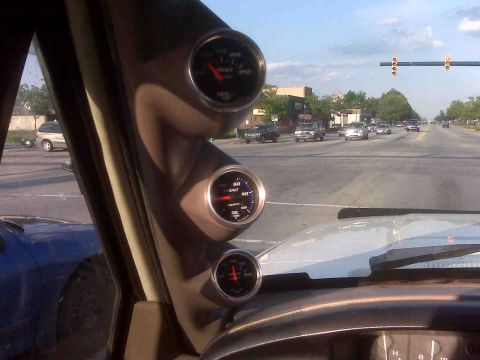 1995 Ford Bronco - Gauges are visible inside a vehicle, with a street and other cars seen through the windshield.
