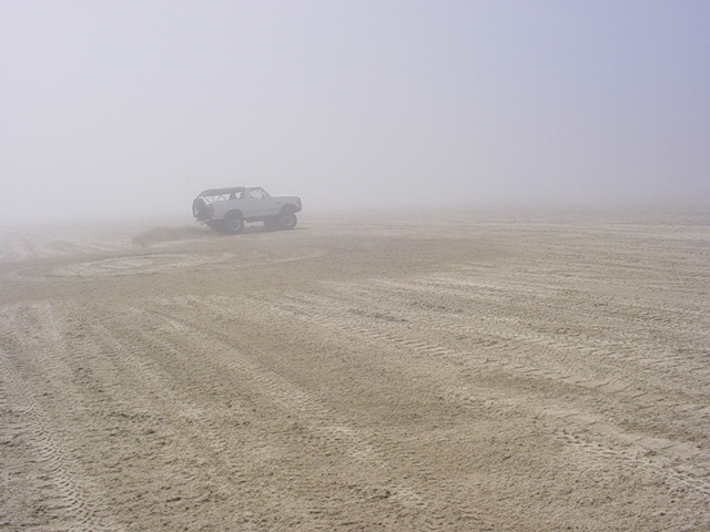 White lifted 4x4 parked alone on a foggy tire-tracked beach