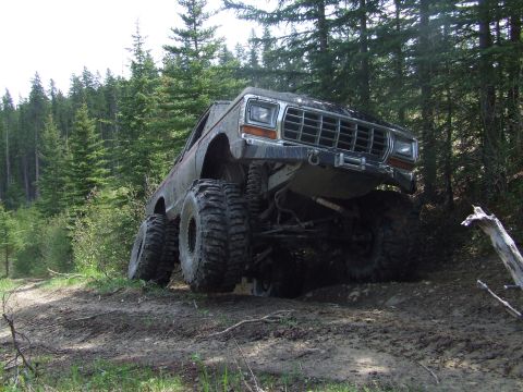 1990 Ford Bronco - This heavily modified truck navigates a muddy trail through a dense forest.