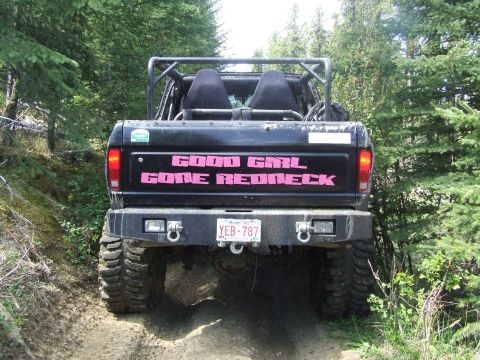 1990 Ford Bronco - A modified black Ford Bronco with 'GOOD GIRL GONE REDNECK' on the tailgate drives on a dirt path.