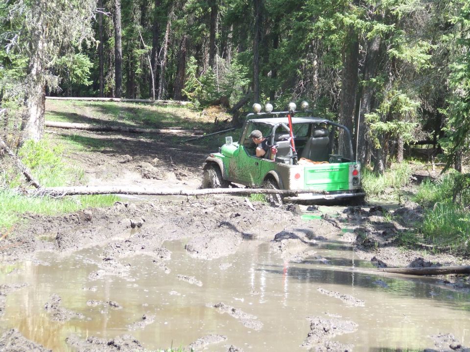 Green off-road vehicle driving through a muddy trail in a forest