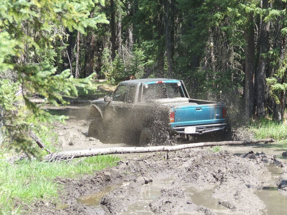 Teal pickup truck splashing mud while driving through a muddy trail in a forest