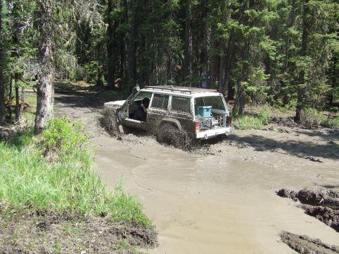 1990 Ford Bronco - Four-door Jeep Cherokee XJ navigating a muddy trail with its door open.