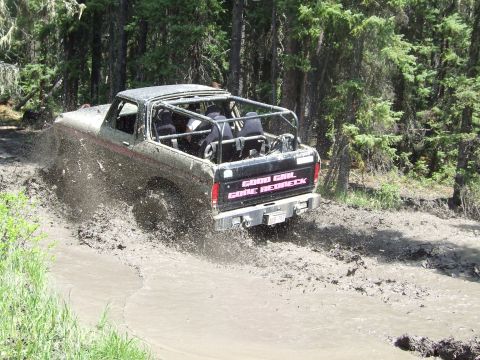 1990 Ford Bronco - This modified Ford Bronco navigates a muddy trail, kicking up a significant amount of spray.