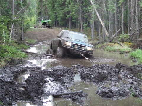 1990 Ford Bronco - An off-road vehicle navigates a treacherous muddy path, using a winch to pull itself through the mire.
