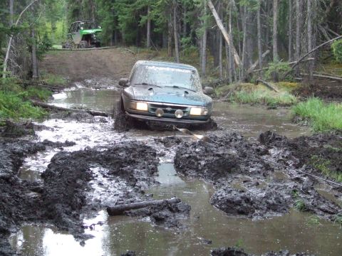 1990 Ford Bronco - A teal SUV navigates a muddy trail, with another vehicle visible in the background.