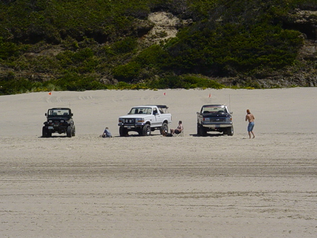 Lifted Jeep Wrangler and two Ford Broncos with whip flags parked on sand dunes