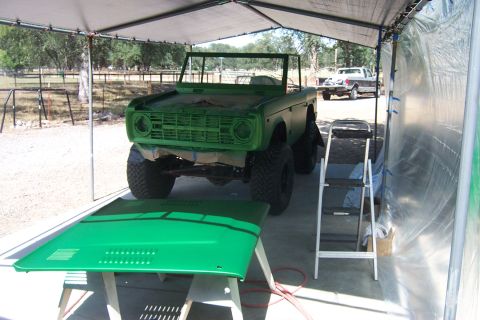 1976 Ford Bronco - A green 1976 Ford Bronco is being painted under a temporary shelter, with its hood removed and placed on sawhorses.
