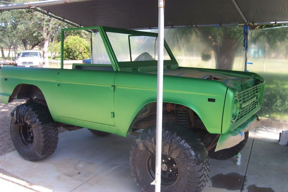 Green 1976 Ford Bronco with large tires, partially painted
