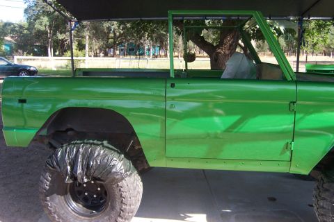 1976 Ford Bronco - Side view of a 1976 Ford Bronco undergoing a bright green paint job, wheels are covered.