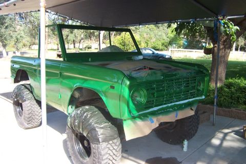 1976 Ford Bronco - A green 1976 Ford Bronco is parked under a canopy, with its tires covered and fresh paint applied.