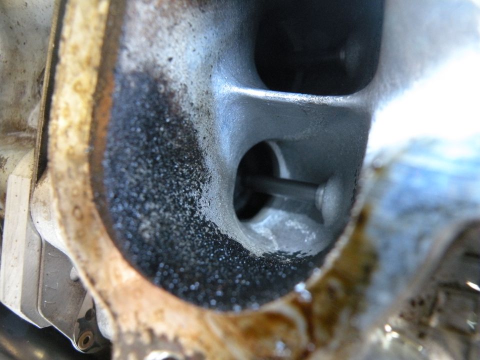 Close-up of an engine intake port with carbon buildup and a valve stem visible