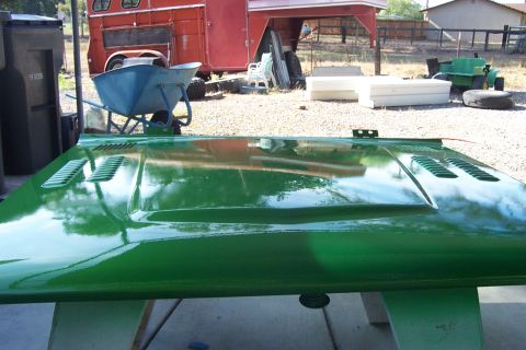 1976 Ford Bronco - A freshly painted green car hood with vents is displayed outdoors.