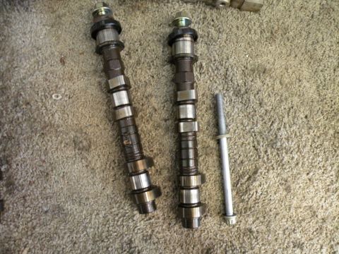 1998 Subaru Legacy - Two camshafts and a bolt are displayed on a carpeted surface, suggesting engine work.