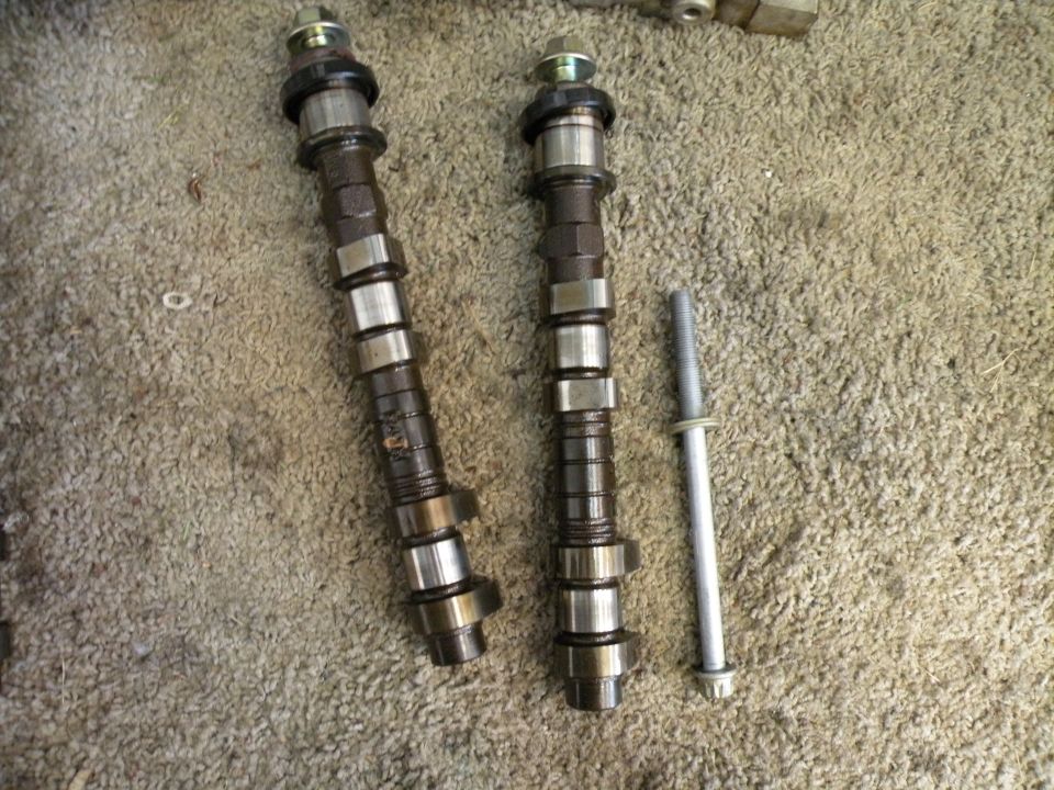 Two camshafts and a bolt lie on a carpeted surface