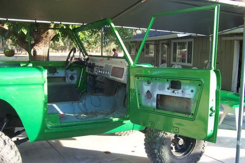 1976 Ford Bronco - The interior of a green 1976 Ford Bronco is visible with both doors open, suggesting it is undergoing restoration or repair.