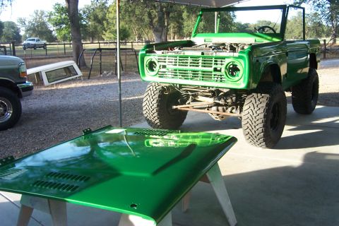 1976 Ford Bronco - A green Ford Bronco is parked outside with its hood removed, possibly undergoing restoration or repair.