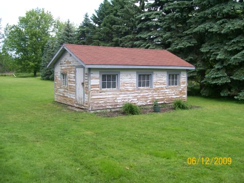 1995 Mercury Grand Marquis - A small detached wood-sided shed or shop building with heavily peeling white paint, a red shingled roof and three windows along the side, s…
