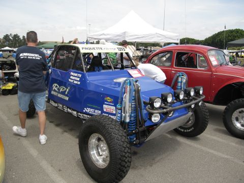1986 Ford Bronco - A custom blue off-road buggy is parked next to a red Volkswagen Beetle at an outdoor event.