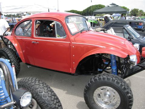 1986 Ford Bronco - A modified red Volkswagen Beetle is parked outdoors, with other vehicles and tents in the background.
