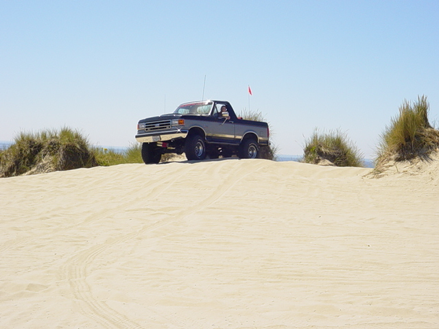 Lifted two-tone Ford Bronco with orange whip flag parked on a sand dune