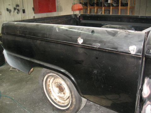 1966 Ford F-100 - The side of a black pickup truck is shown, with evidence of body repairs and a single wheel visible.