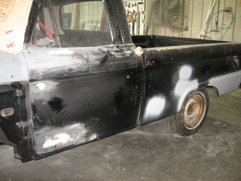 1966 Ford F-100 - This 1966 Ford F-100 pickup truck is in a body shop, with visible primer and sanding marks on its black paint.