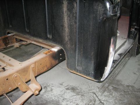 1966 Ford F-100 - The side view of a black truck bed and its rusty frame, showing signs of bodywork on the fender.