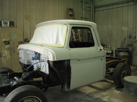 1966 Ford F-100 - A 1966 Ford F-100 pickup truck is shown in a body shop, undergoing repairs or restoration with its cab and chassis exposed.