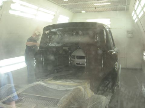 1966 Ford F-100 - A worker sprays a dark 1956 Ford F-100 truck in a paint booth, with another vehicle visible inside.