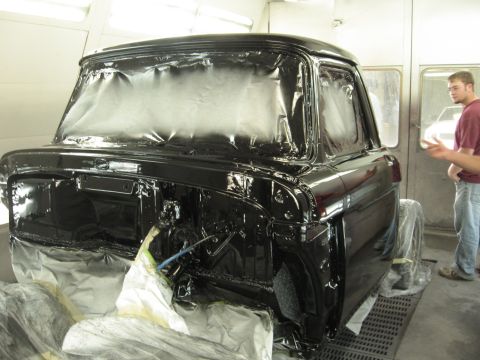 1966 Ford F-100 - A black 1966 Ford F-100 pickup truck is being painted inside a body shop, with its windows covered for protection.