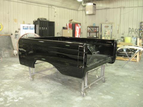 1966 Ford F-100 - A freshly painted black truck bed sits on a stand in a body shop.