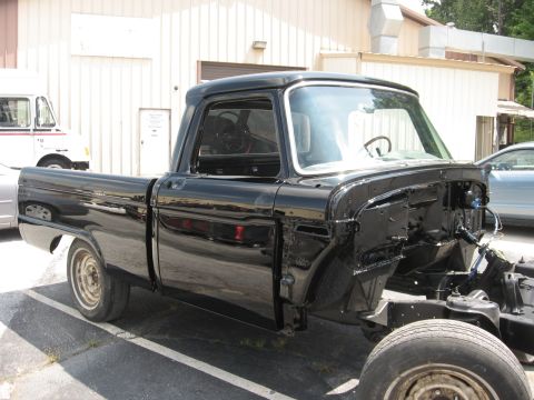 1966 Ford F-100 - A black pickup truck is undergoing repairs, with its front end exposed and engine bay empty.