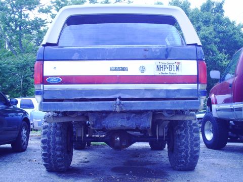 1990 Ford Bronco - This 1990 Ford Bronco features a distinctive red, white, and blue stripe pattern on its rear tailgate and a white camper shell.