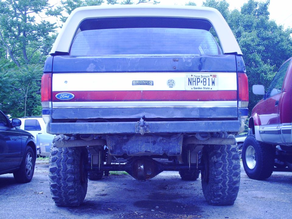 Rear view of a 1990 Ford Bronco with a white camper shell and red, white, and blue stripes