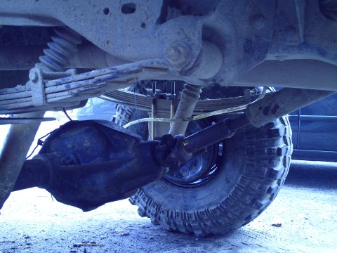 1990 Ford Bronco - The underside of a vehicle shows its rear axle, suspension components, and a large off-road tire.