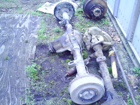 1990 Ford Bronco - Several vehicle axles and suspension components are laid out on the ground, some with drum brakes visible.