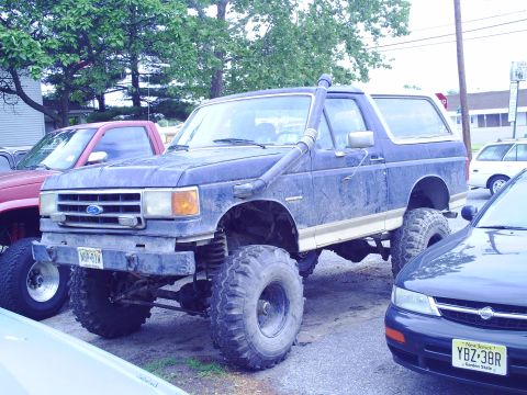 1990 Ford Bronco - A modified blue Ford Bronco is parked next to other vehicles.