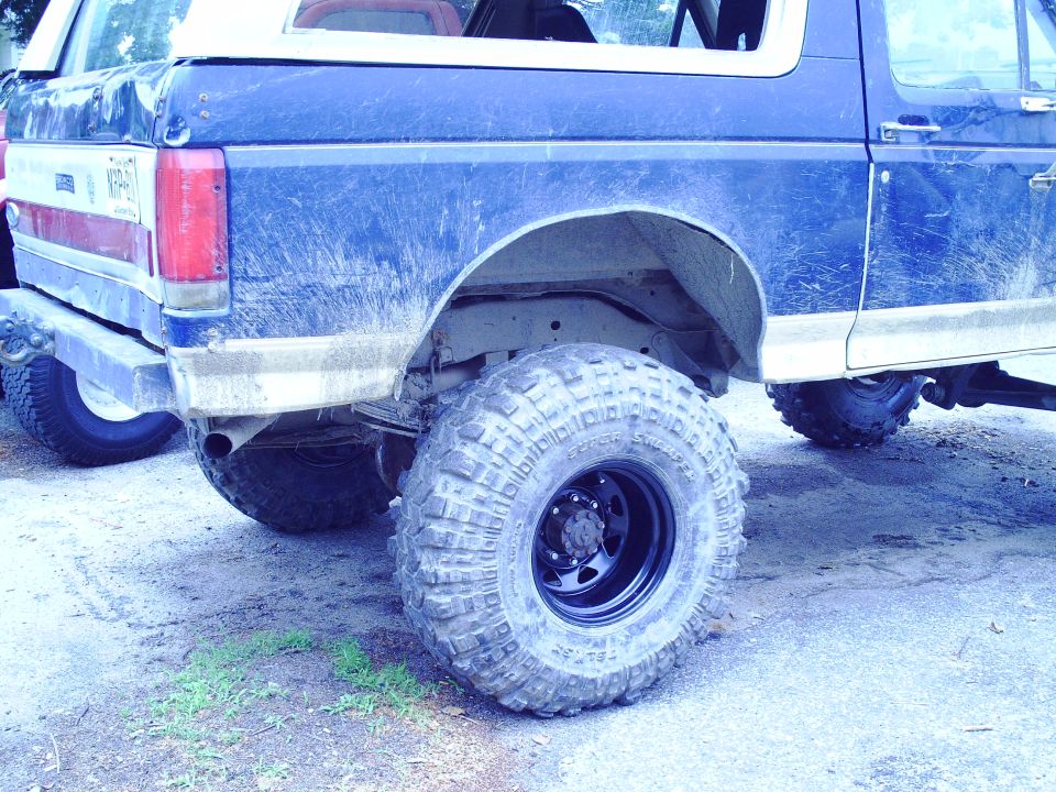 Blue Ford Bronco rear quarter panel with large off-road tires and white roof trim