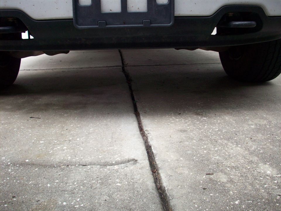 Underside view of a vehicle's rear bumper and tires on a concrete driveway