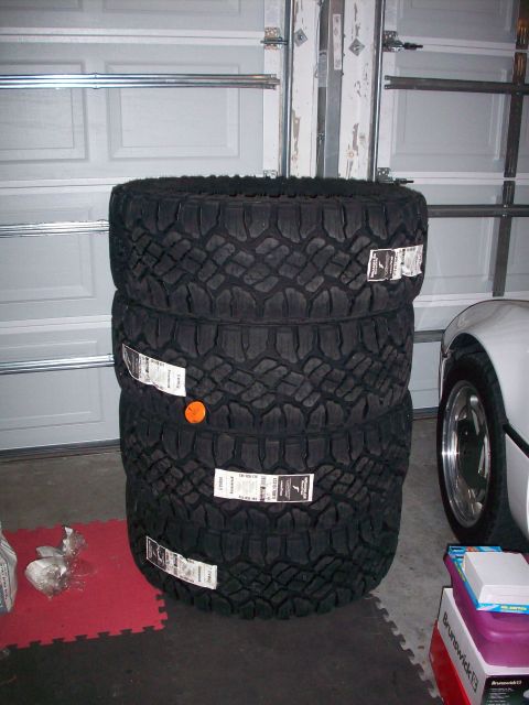 2006 Ford F-150 - A stack of four new off-road tires with tags attached, sitting in a garage next to a white vehicle.