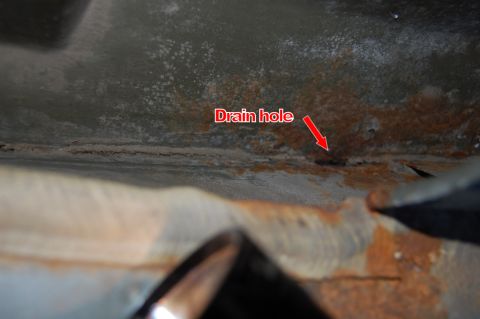 1985 Mercury Grand Marquis - Close-up view of a rusted metal surface with a drain hole indicated by a red arrow and text.