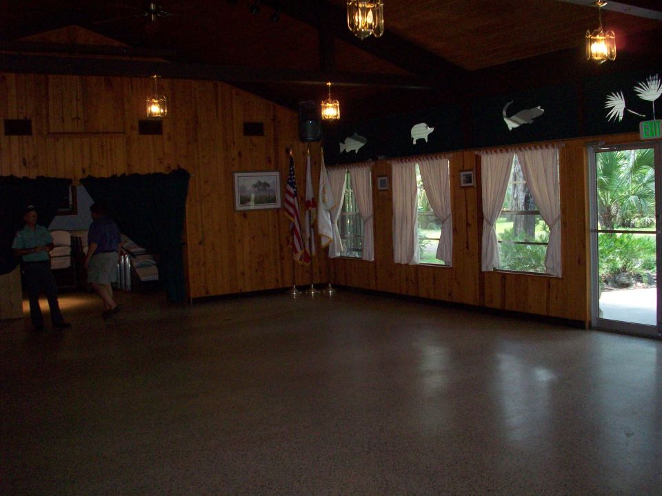 Interior of a room with wood paneling, windows, flags, and two people standing near a curtained area